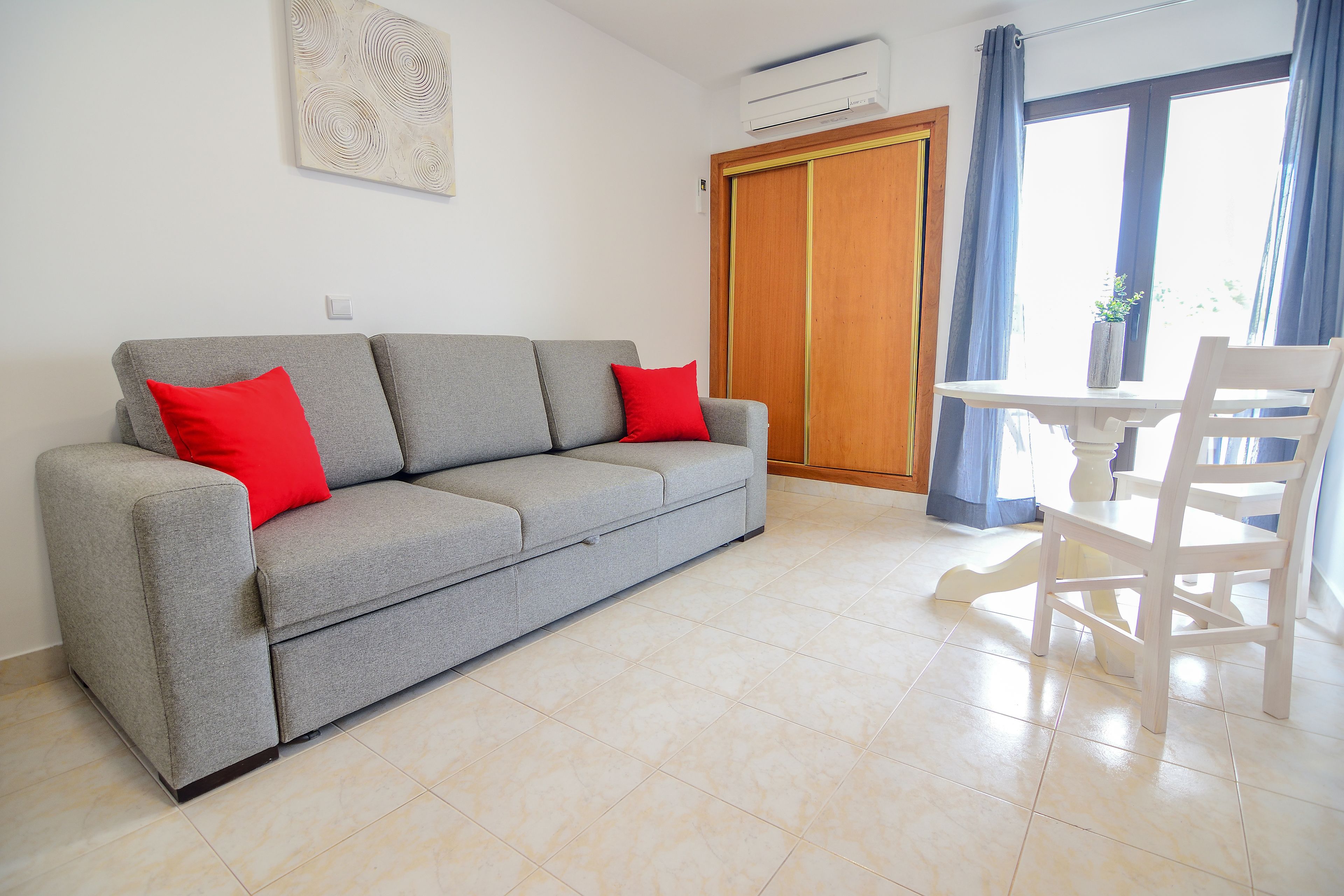 A modern living room with a grey sofa, red cushions, a white table, and a wooden door.