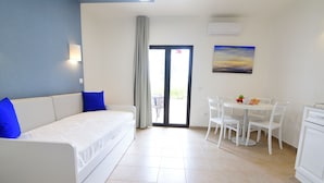 Une chambre d’hôtel moderne comprenant un lit, une table à manger avec des chaises, un tableau au mur et une porte-fenêtre coulissante donnant sur un espace extérieur.
