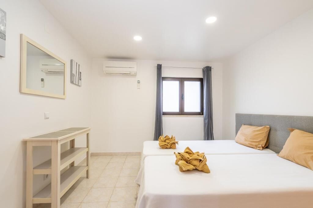 Hotellihuone, jossa on kaksi sänkyä, työpöytä, peili ja ilmastointilaite.