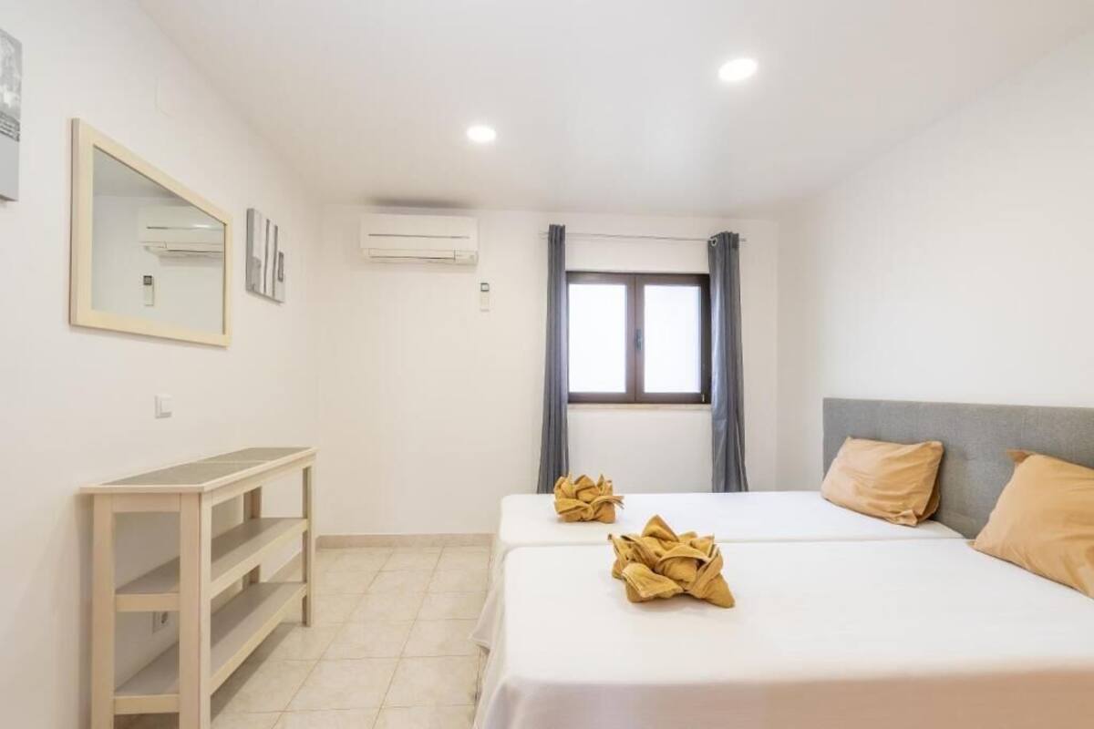 A hotel room with two beds, a desk, a mirror, and an air conditioning unit.