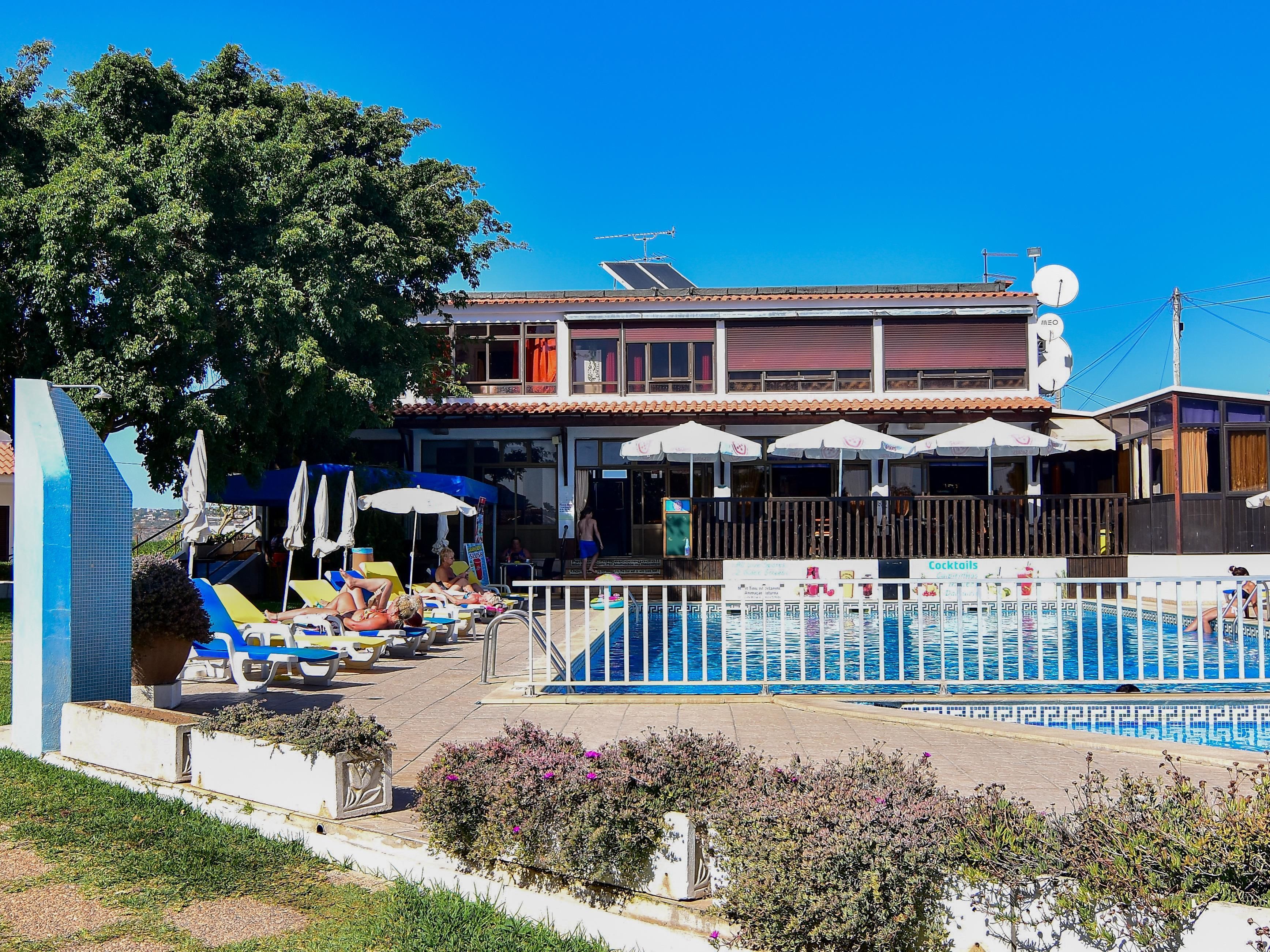 A hotel with a swimming pool, sun loungers, and umbrellas.