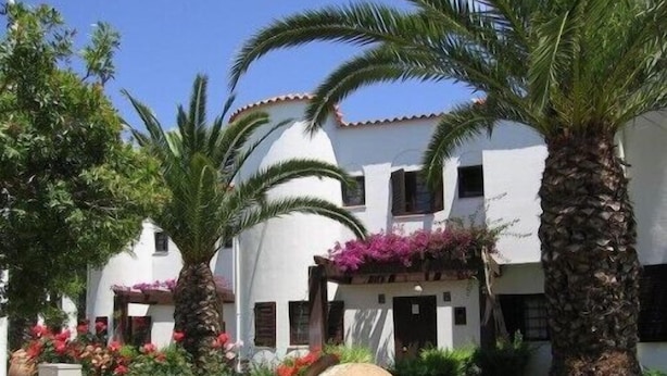 Un bâtiment blanc doté de nombreux balcons, entouré de palmiers et de plantes en fleurs.