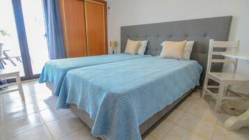 Una cama doble con cabecera gris, dos mesitas de noche y un armario de madera.