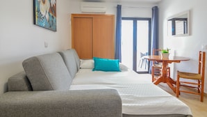 Une pièce moderne avec un canapé gris, une armoire en bois, une table à manger avec des chaises et une fenêtre avec des rideaux.