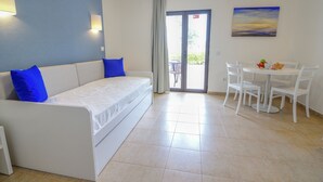 Ein modernes Zimmer mit einem weißen Sofa, blauen Kissen, einem Esstisch mit Stühlen und einem Gemälde an der Wand.