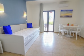Ein modernes Zimmer mit einem weißen Sofa, blauen Kissen, einem Esstisch mit Stühlen und einem Gemälde an der Wand.