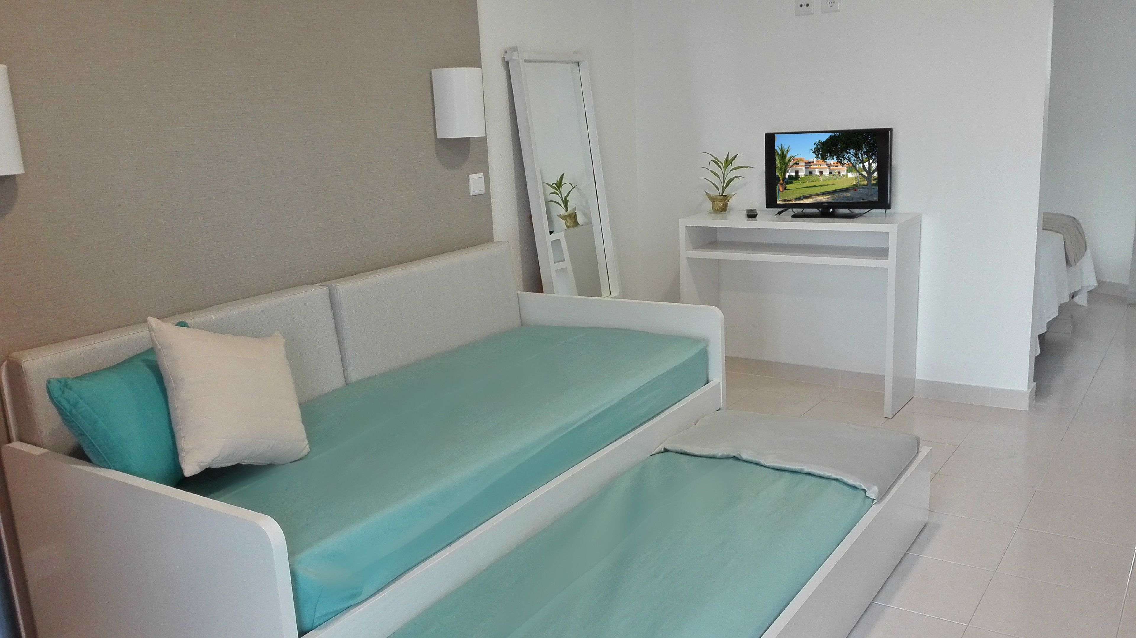 Una habitación pequeña y moderna con una cama individual, un televisor sobre un mueble, una escalera y una planta pequeña.