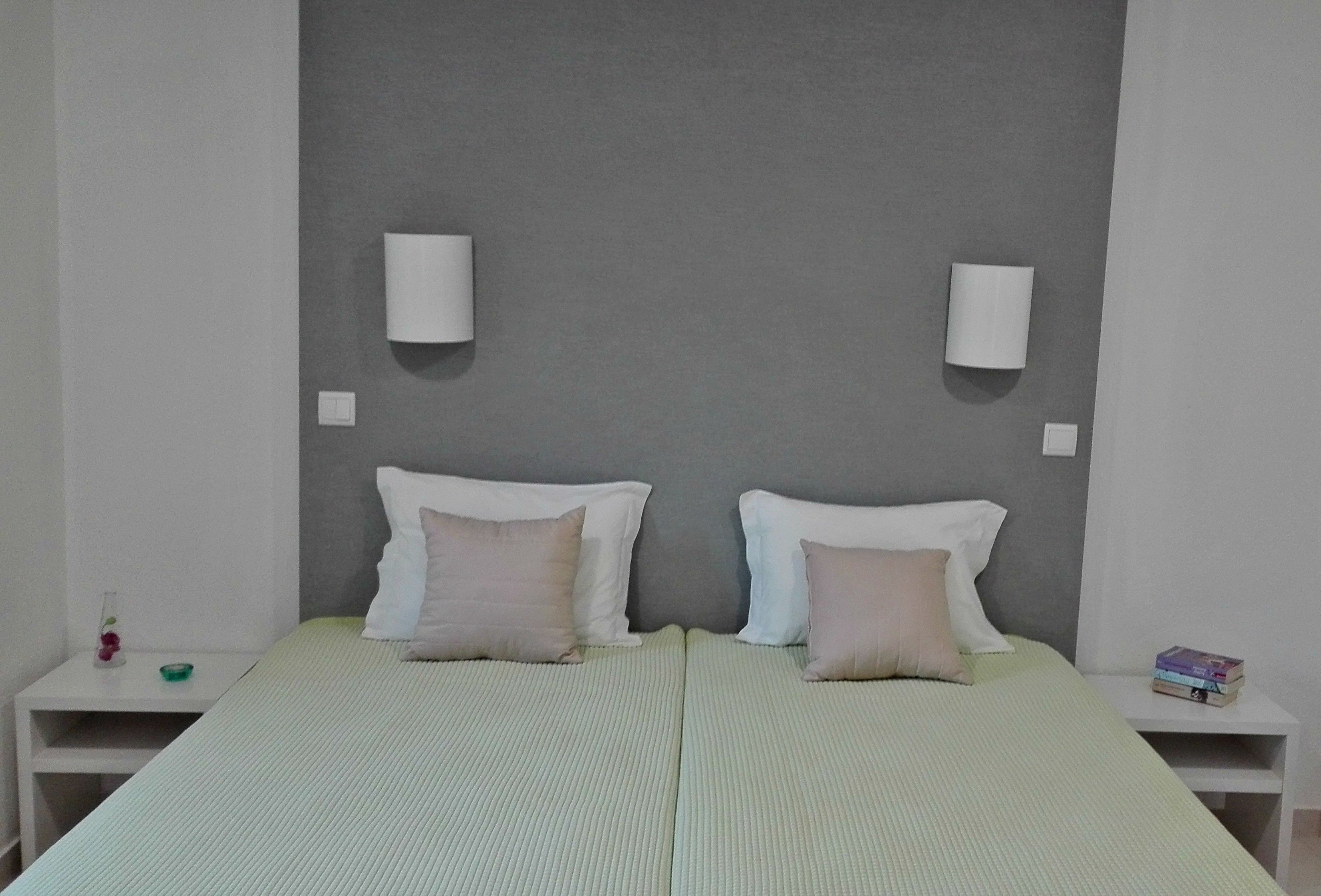 Una cama doble con dos almohadas, una mesita de noche con un libro y una lámpara de pared.