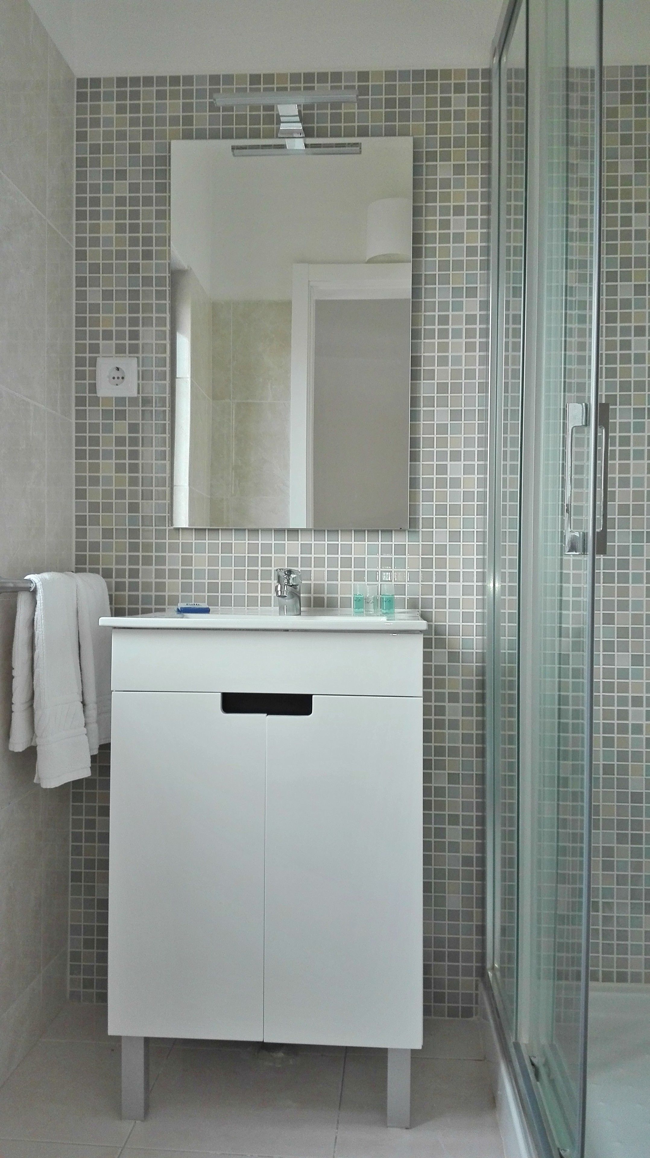 A bathroom with a white vanity, a mirror, and a glass shower enclosure.