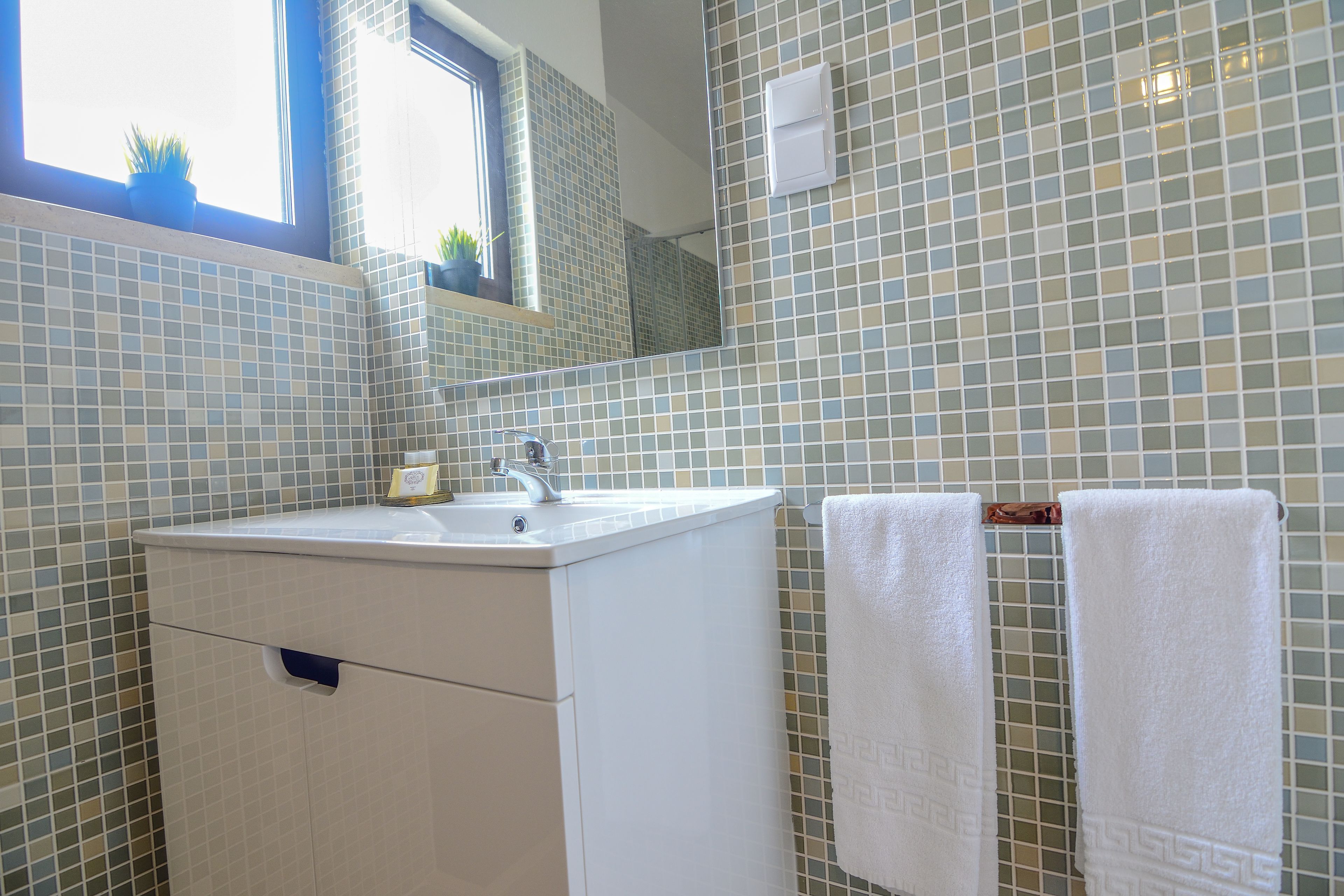 Ein Badezimmer mit einem weißen Waschbecken, einem Spiegel und zwei Handtüchern an einem Haken.