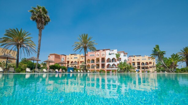 A hotel with a pool, palm trees, and a clear blue sky. - Jardim Da Meia Praia Hotel (Lagos)