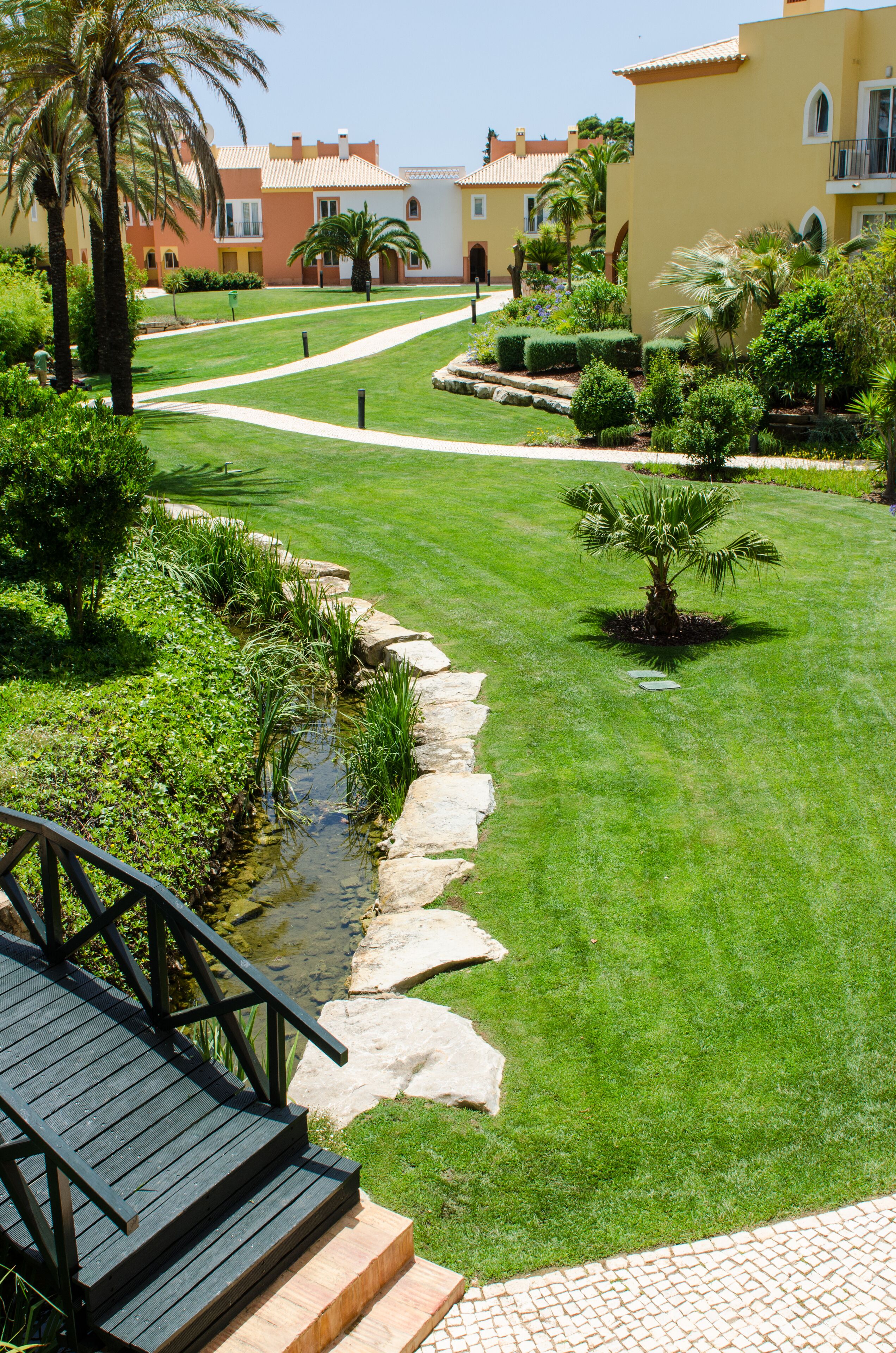 Un jardin bien entretenu, agrémenté d’un petit élément décoratif aquatique, de marches en pierre et d’une terrasse en bois.