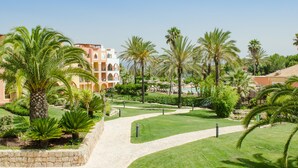 A landscaped garden with palm trees, a pathway, and a building with balconies. - Jardim Da Meia Praia Hotel (Lagos)