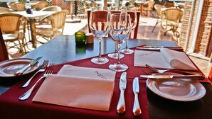A table set for dining with wine glasses, cutlery, and plates, with a view of outdoor seating. - Jardim Da Meia Praia Hotel (Lagos)