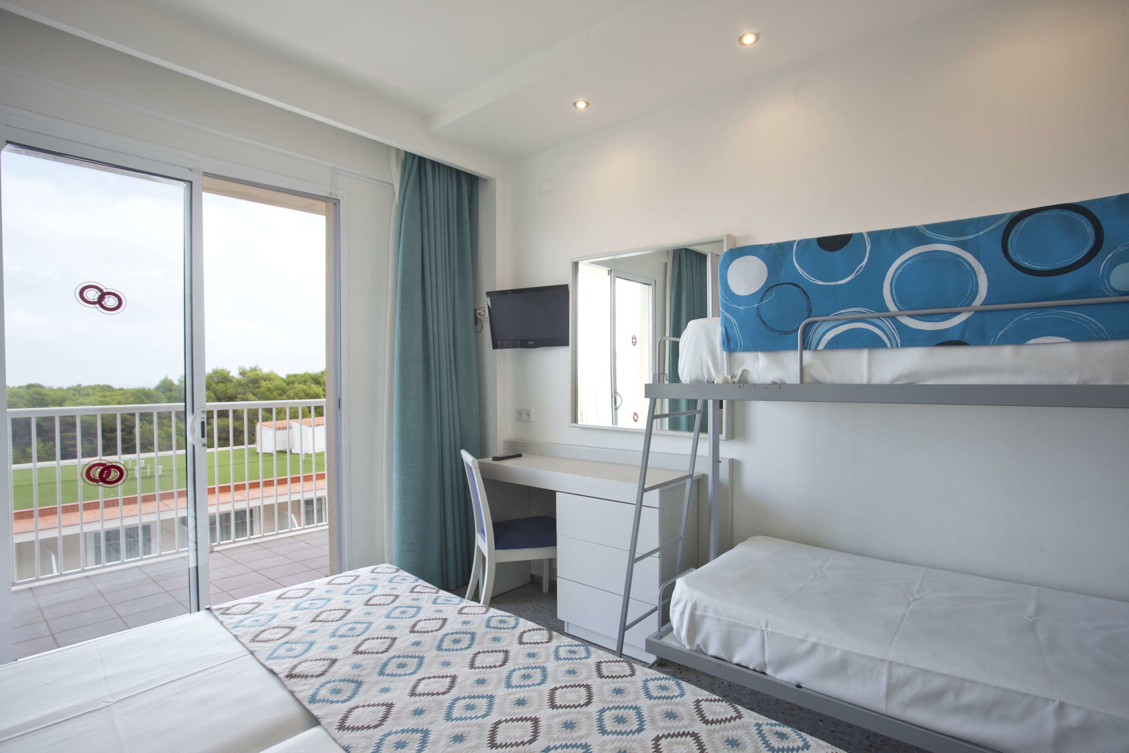 A hotel room with a balcony, a bed, a desk, and a TV.