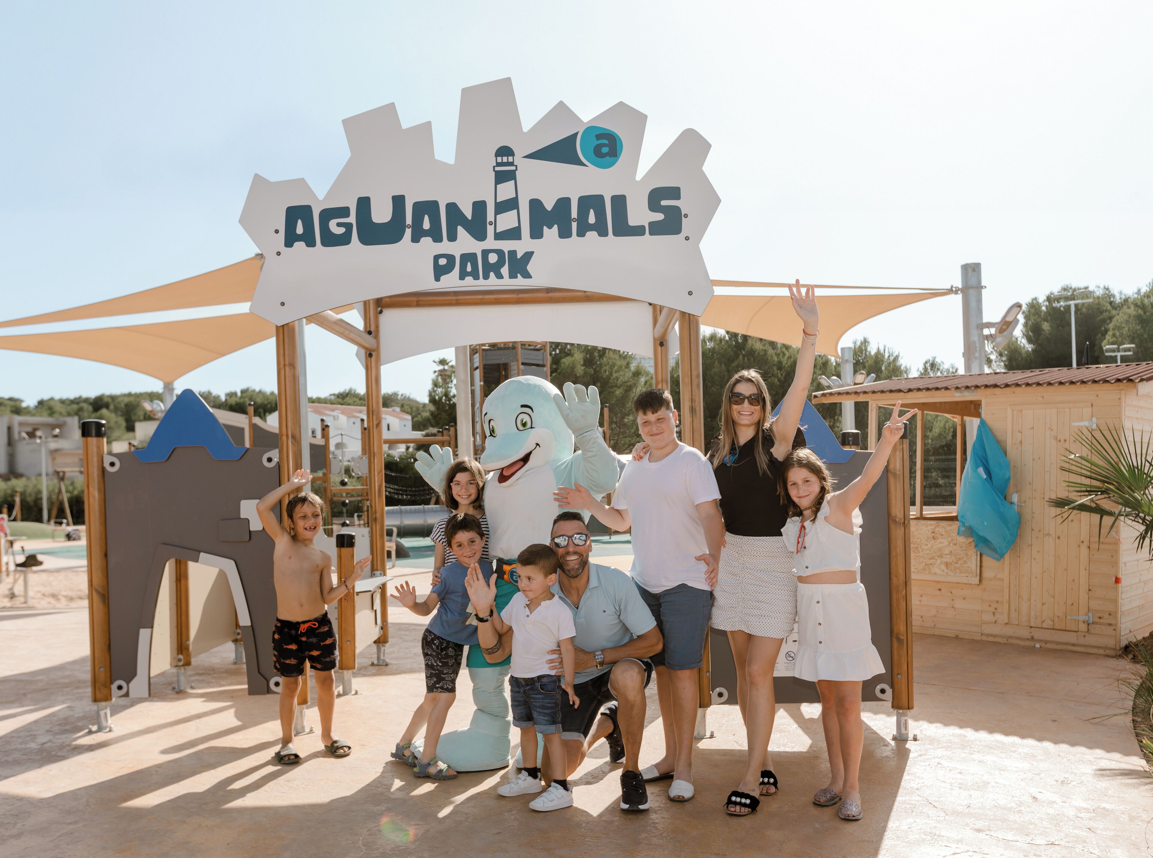 Un groupe de personnes se trouve à l’entrée du parc d’Aguanmals, devant une grande enseigne représentant un phare, qui sert de mascotte.