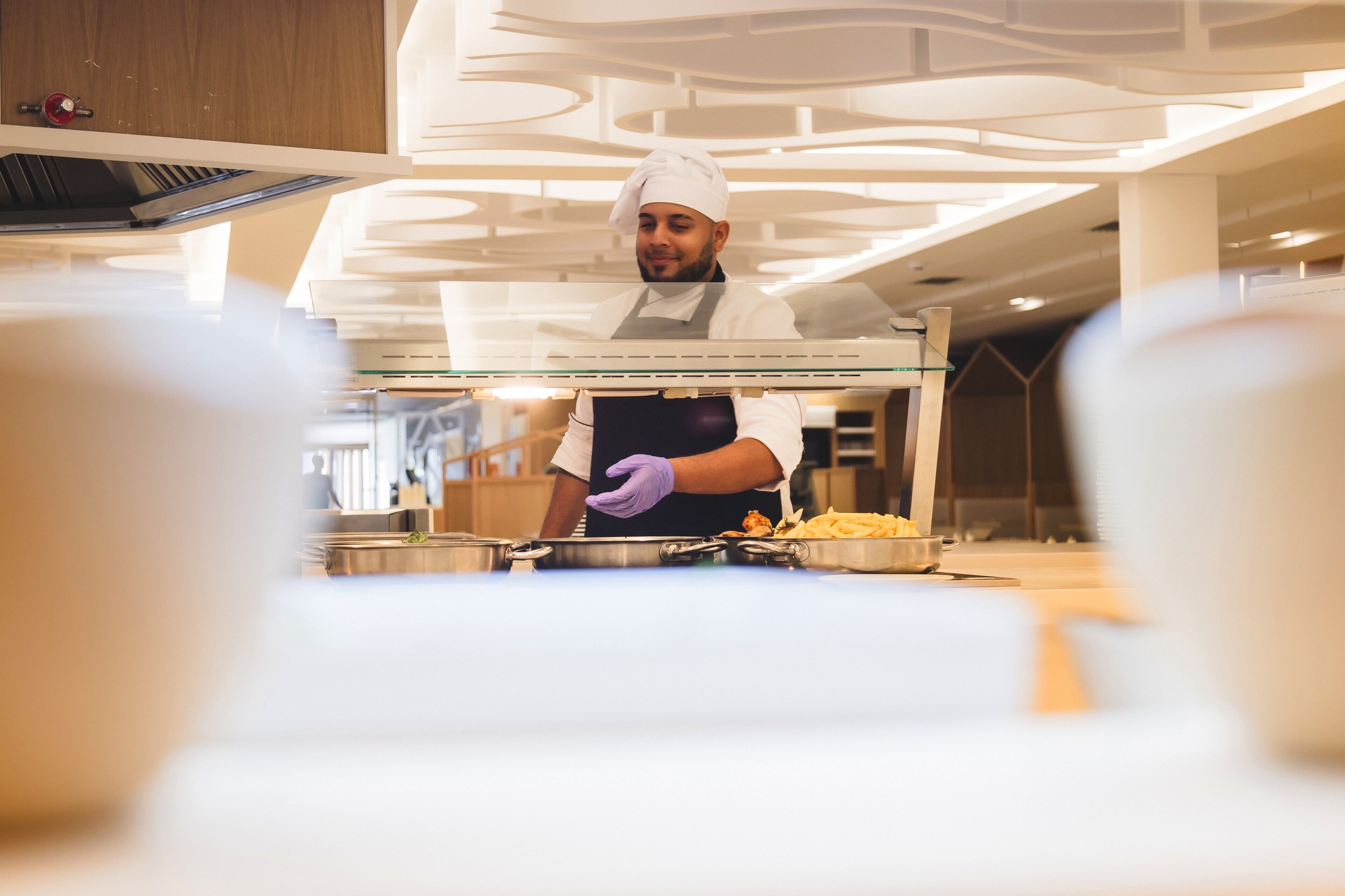 A chef in a professional kitchen with stainless steel counters and a modern ceiling design.
