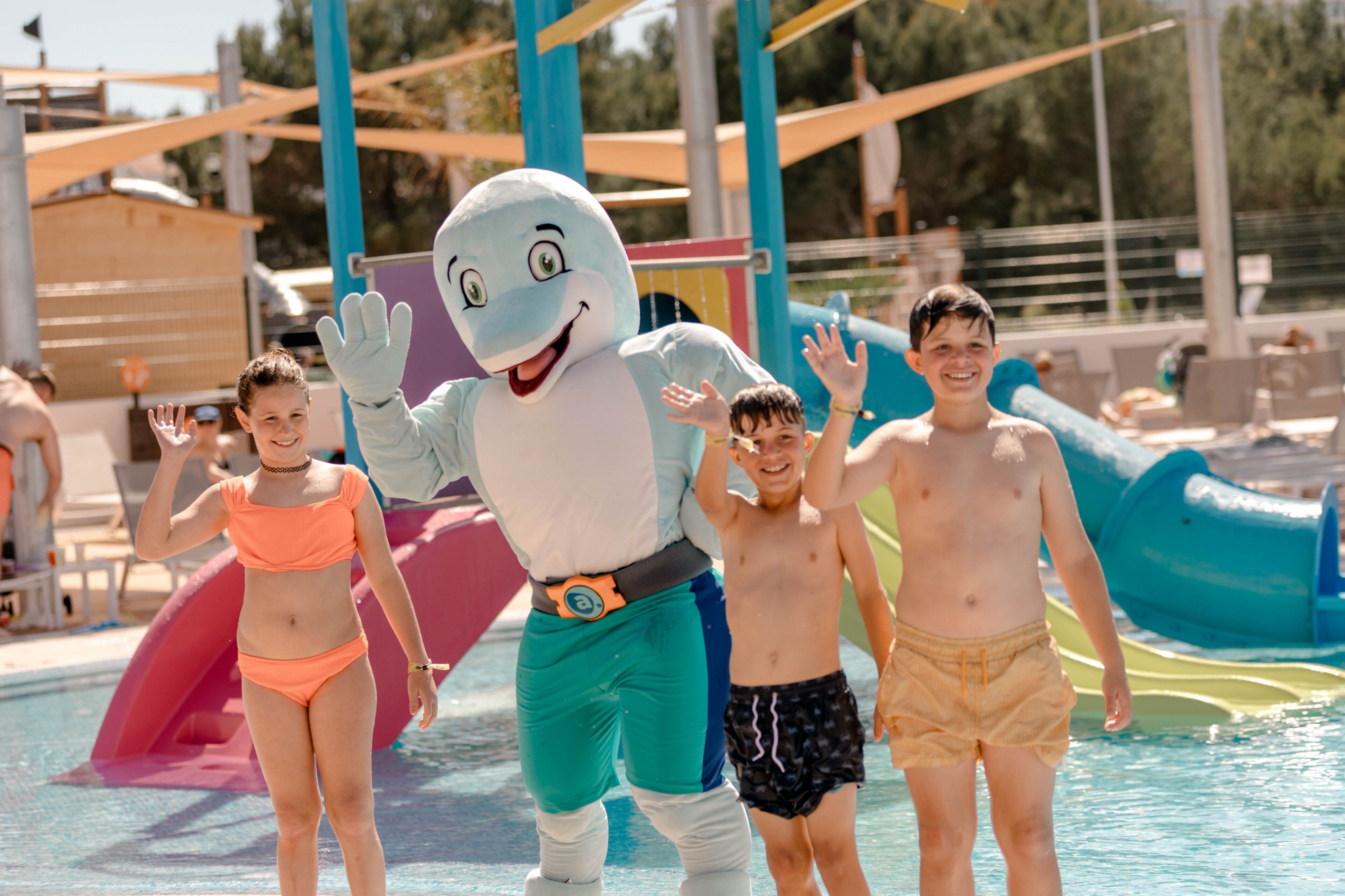 Een mascotte in een zwembadgedeelte, omringd door kinderen en volwassenen.