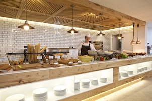 Montaje de bufé con diversos alimentos y utensilios, un chef con uniforme y un fondo de pared de ladrillo.