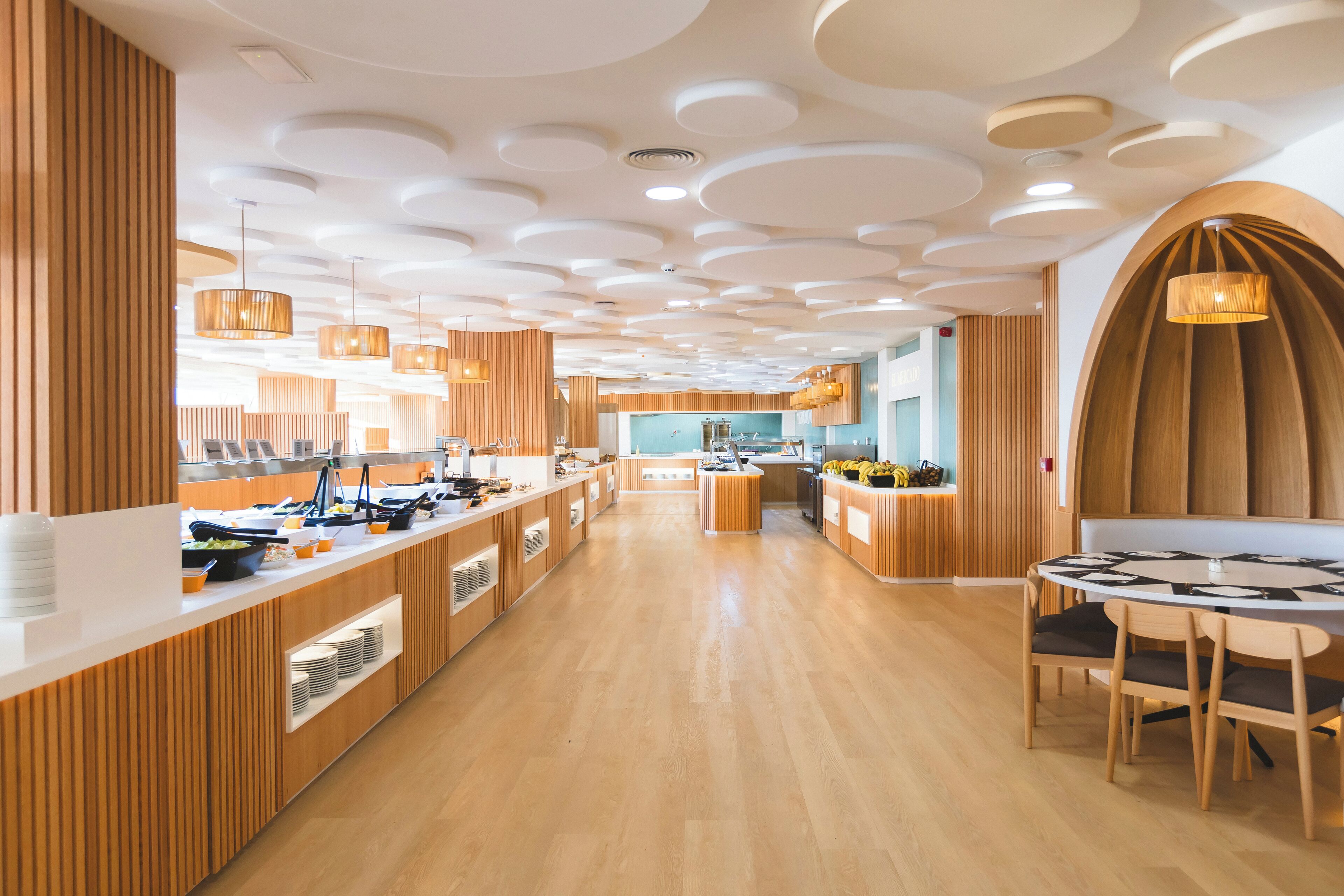 Un restaurante moderno con paneles de madera, un comedor central y una cocina al fondo.