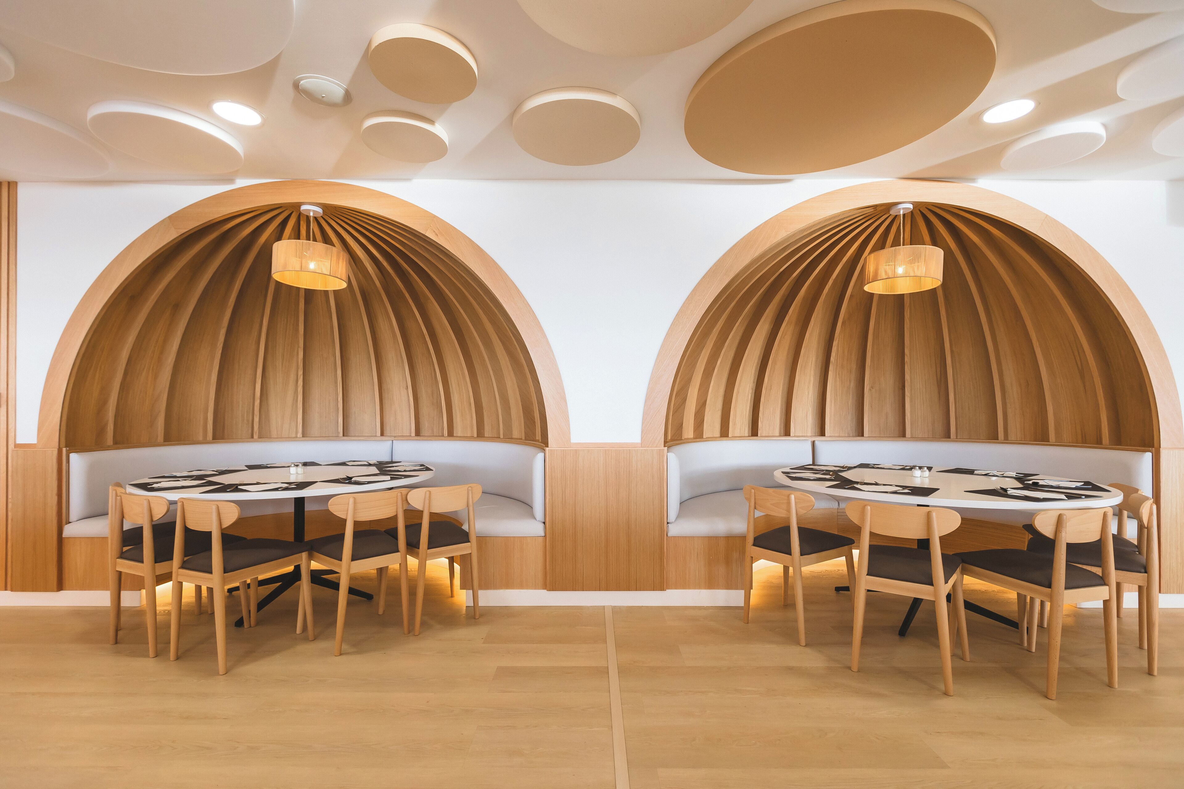 A modern dining area with a round table and chairs, wooden panel walls, and recessed lighting.