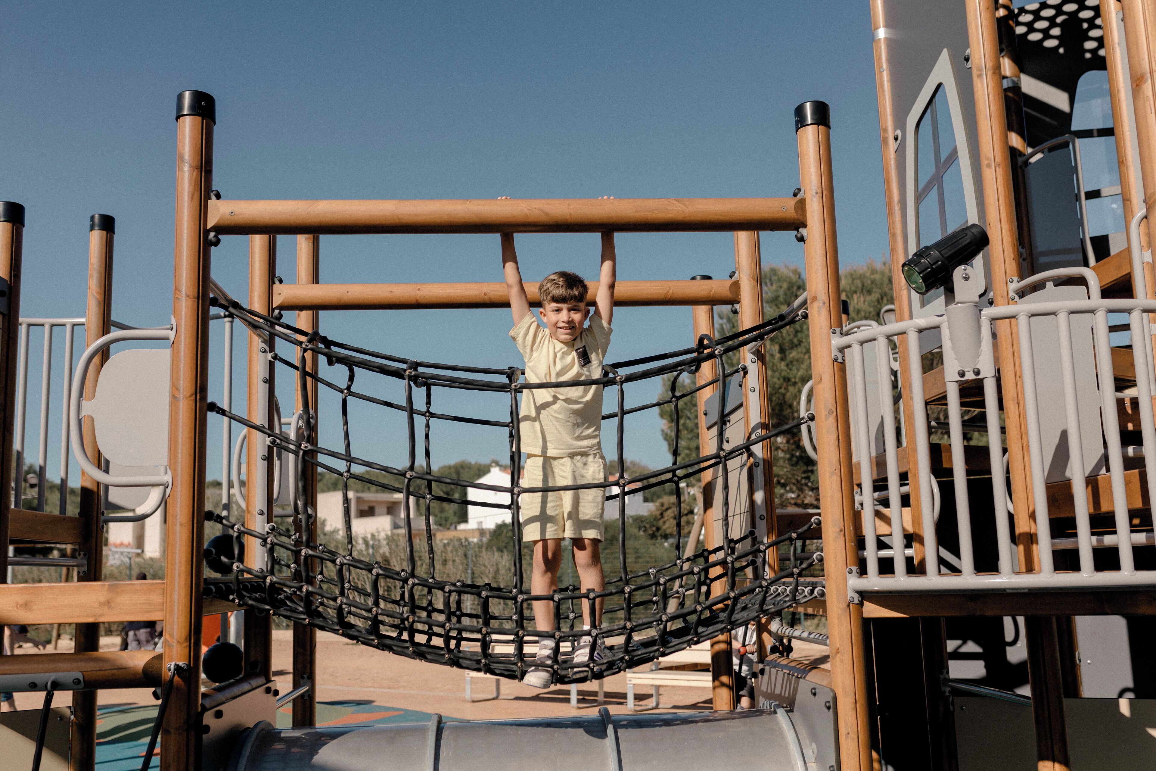 A child on a playground structure with a net bridge and metal bars.
