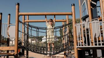 A child on a playground structure with a net bridge and metal bars.