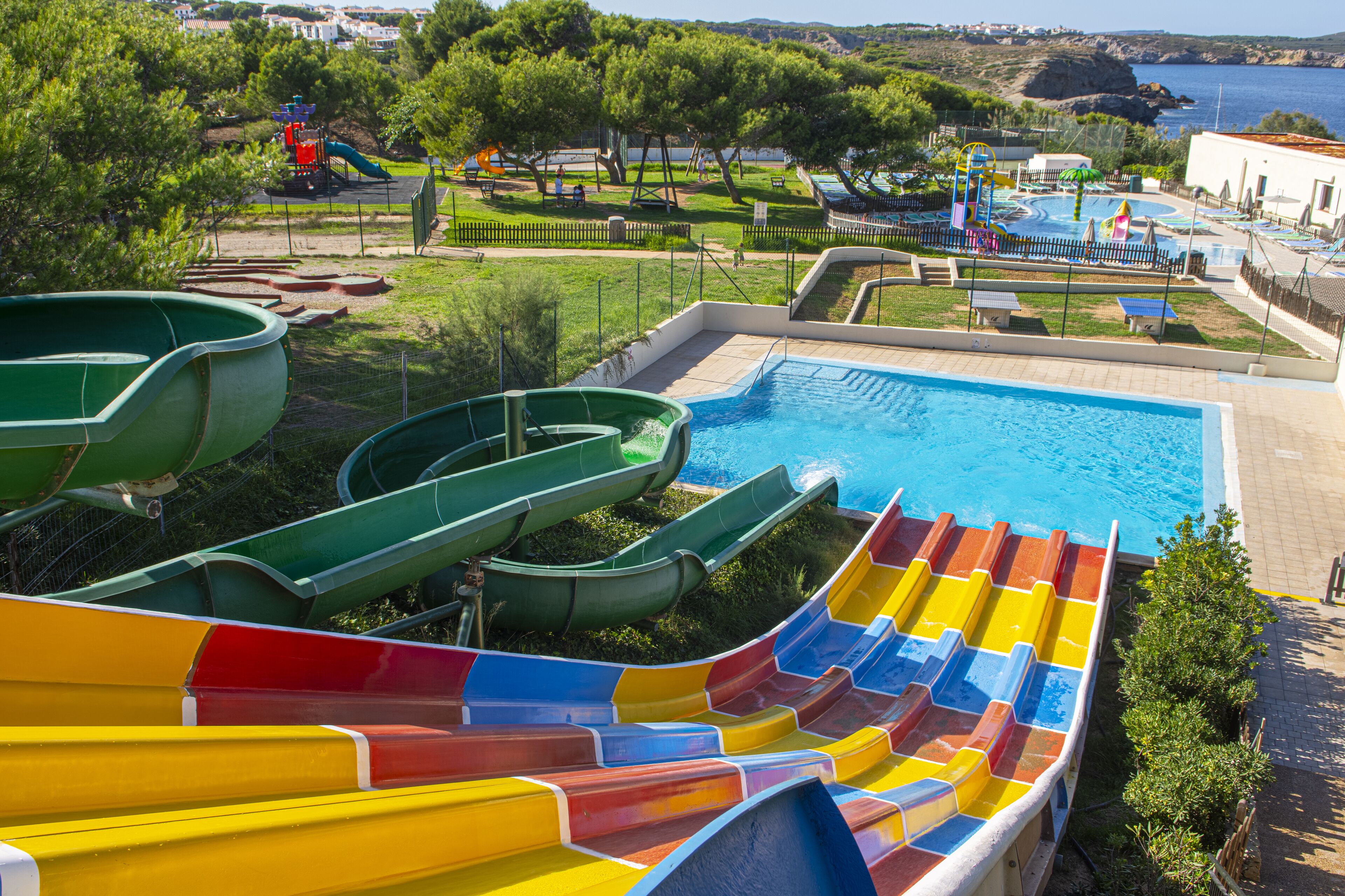Una piscina con varias toboganes, rodeada de vegetación y vistas al mar.