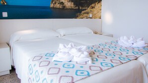 Quarto de hotel com cama, mesa de cabeceira e televisão na parede exibindo uma paisagem costeira.