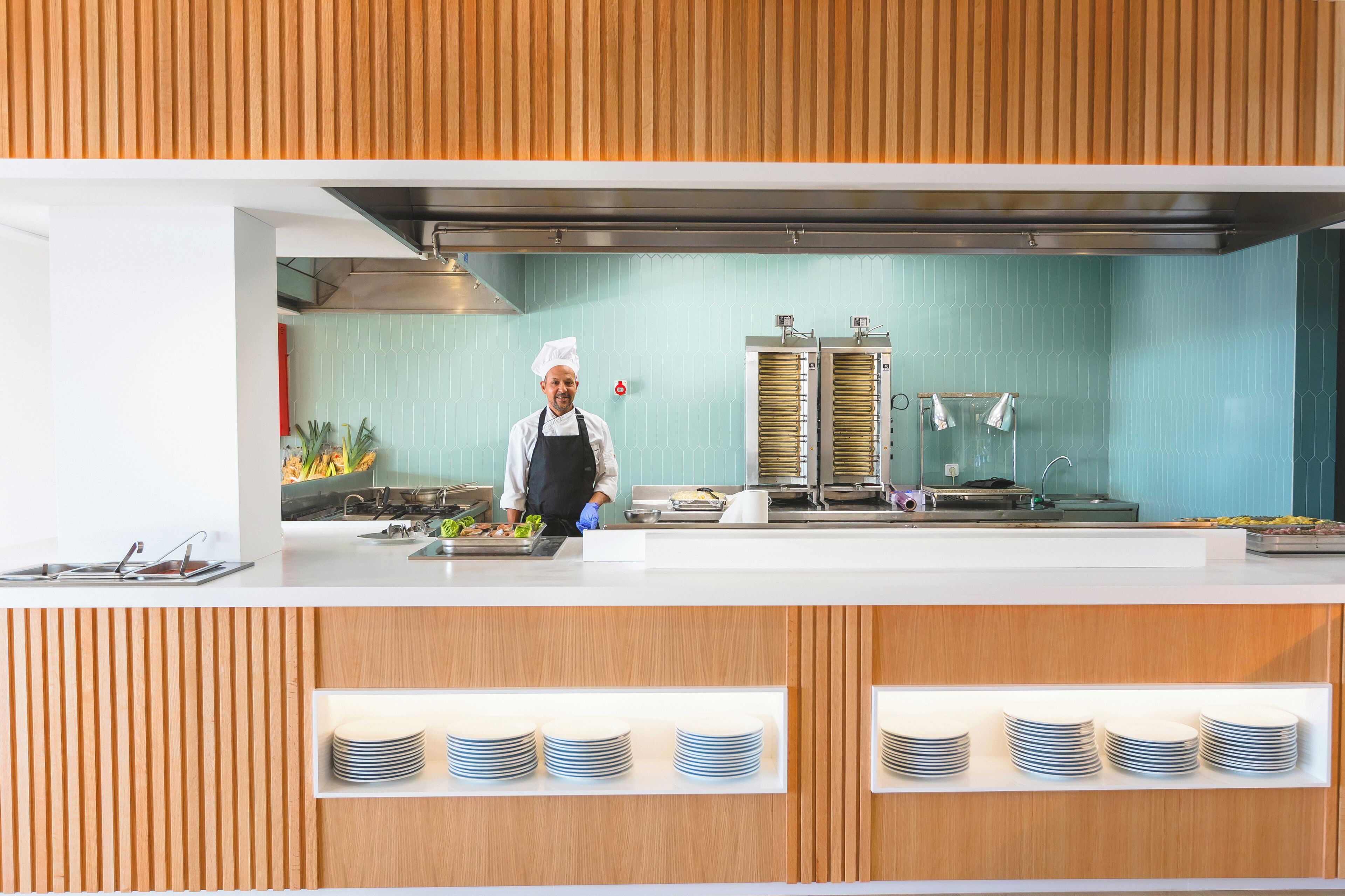 A modern kitchen with a chef preparing food, a stainless steel range hood, and a blue tiled backsplash.