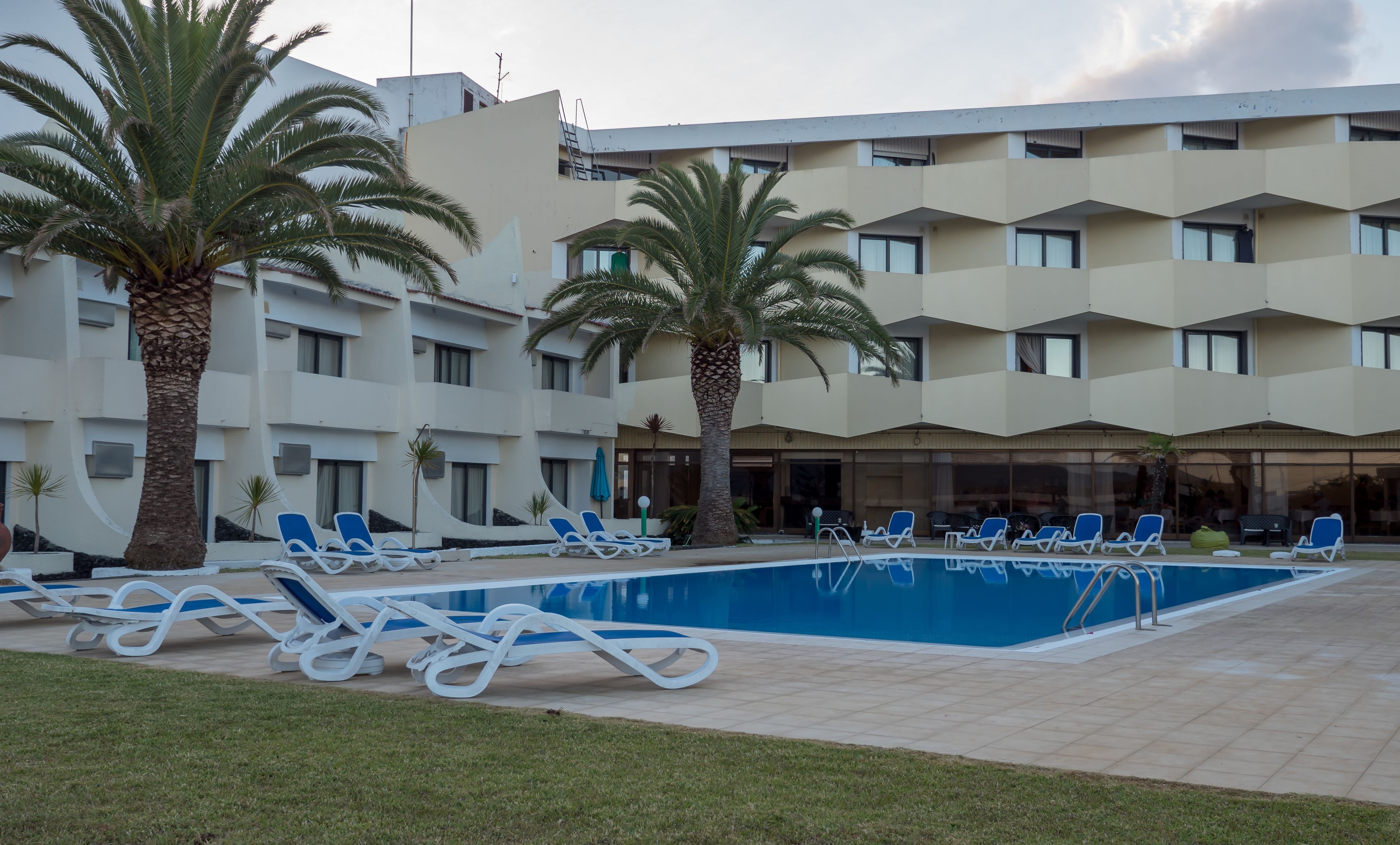 A hotel with a swimming pool, lounge chairs, and palm trees.