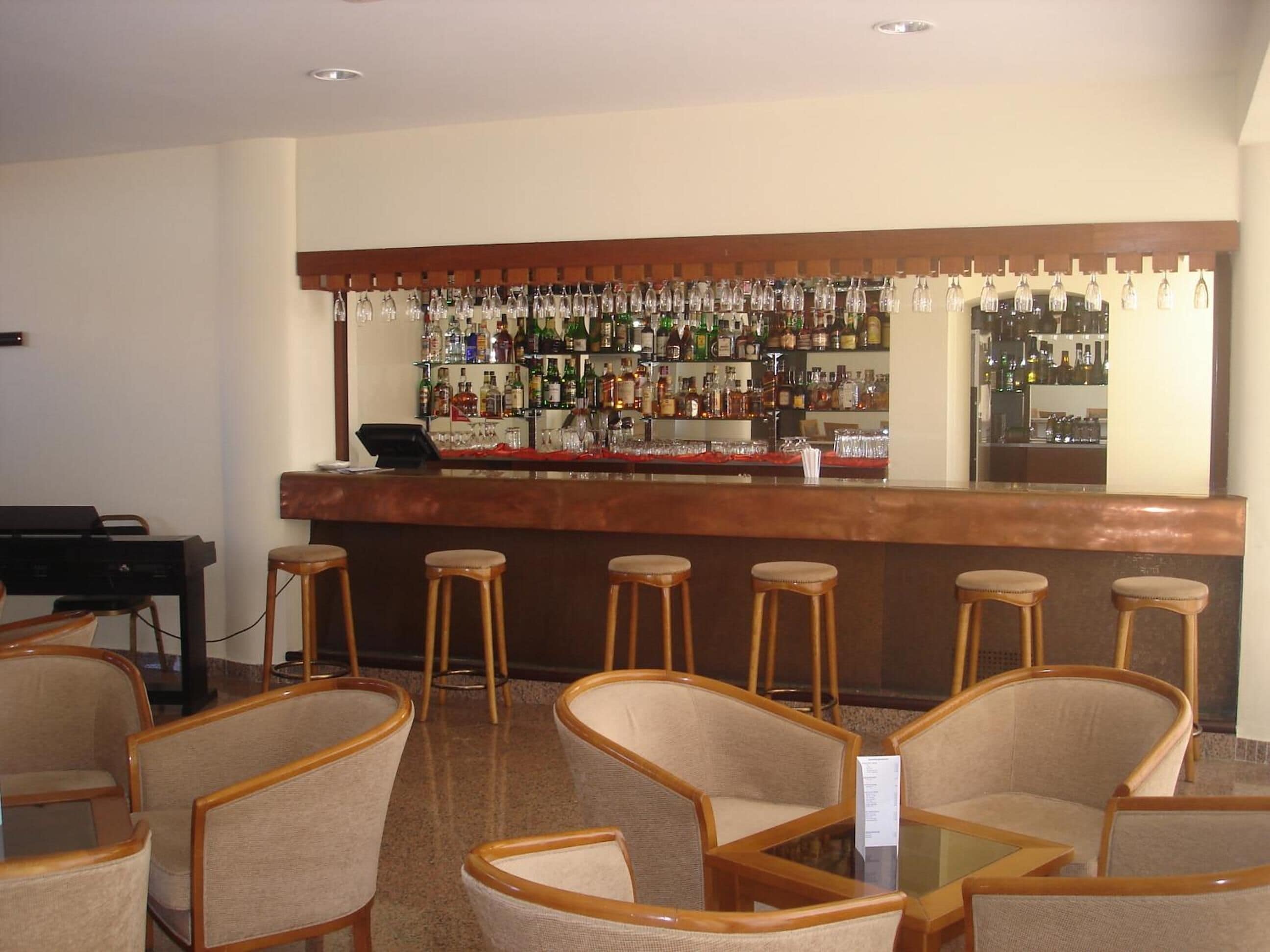 A bar area with a long counter, multiple stools, and a piano.