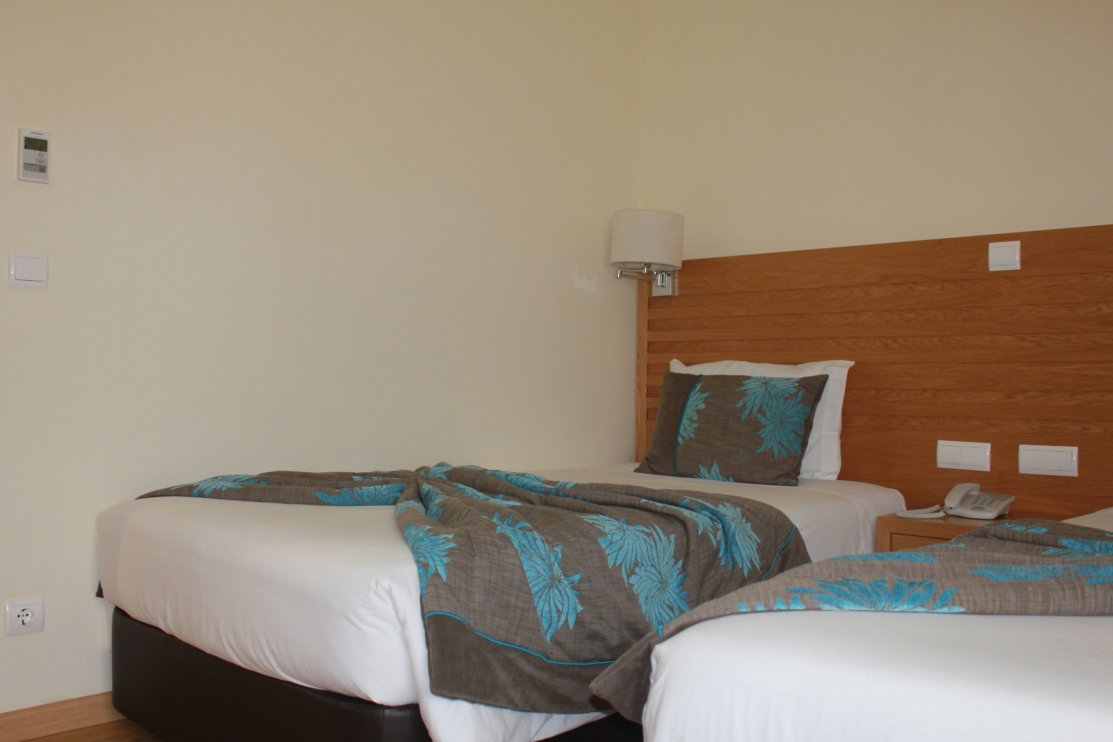A hotel room with two beds, a wooden headboard, a bedside table with a phone, and a wall-mounted lamp.