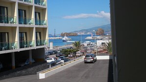 A multi-story hotel with balconies overlooking a coastal road with parked cars and a boat in the background. - Hotel Caravelas (Madalena)