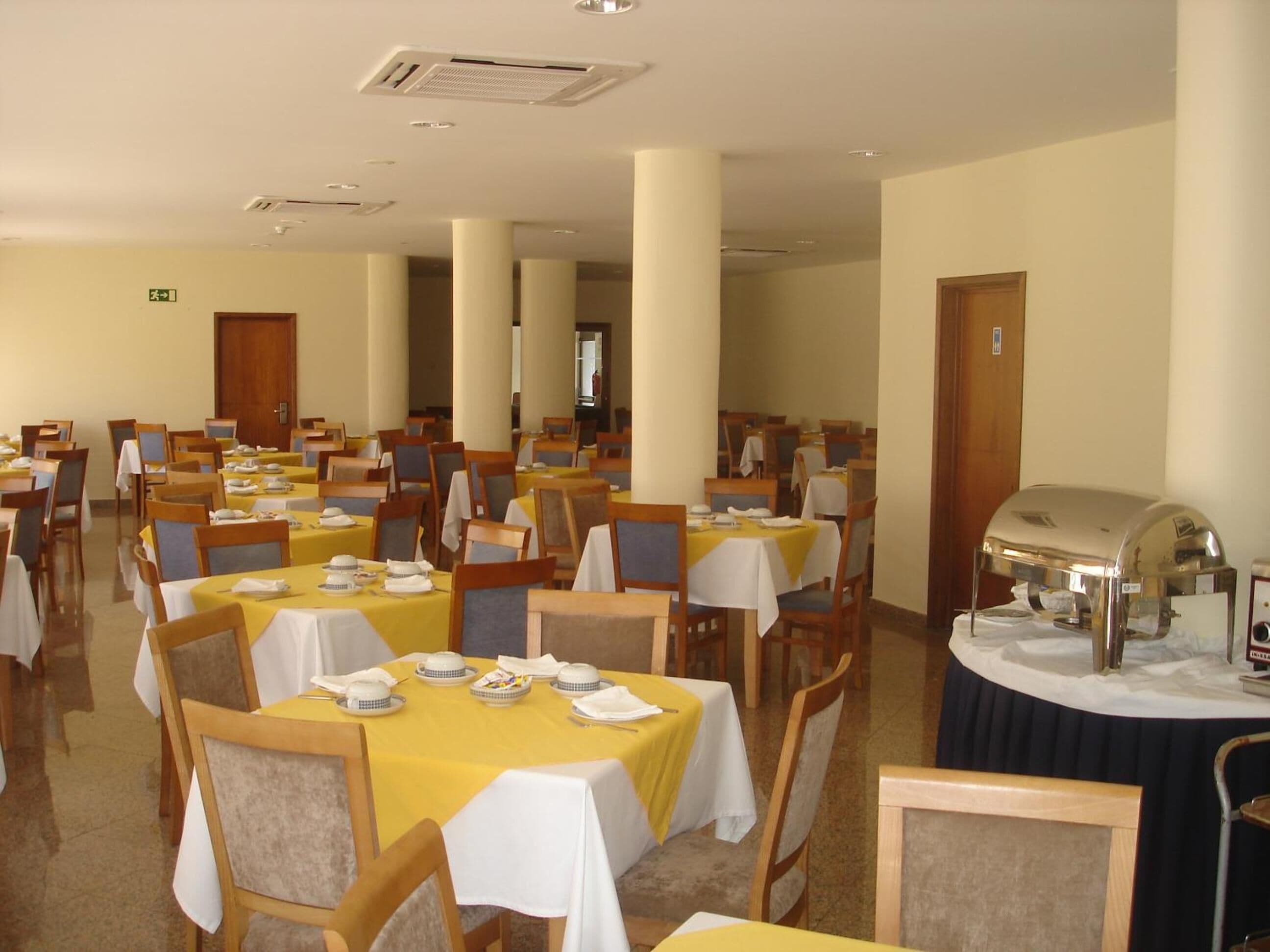 A spacious dining area with multiple tables set for meals, a grill station, and a visible exit sign.