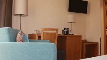 A hotel room with a bed, a desk, a chair, a TV, and a lamp.