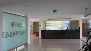 Zona de recepción de un hotel con mostrador de mármol, una recepcionista y un ventanal con vistas panorámicas.