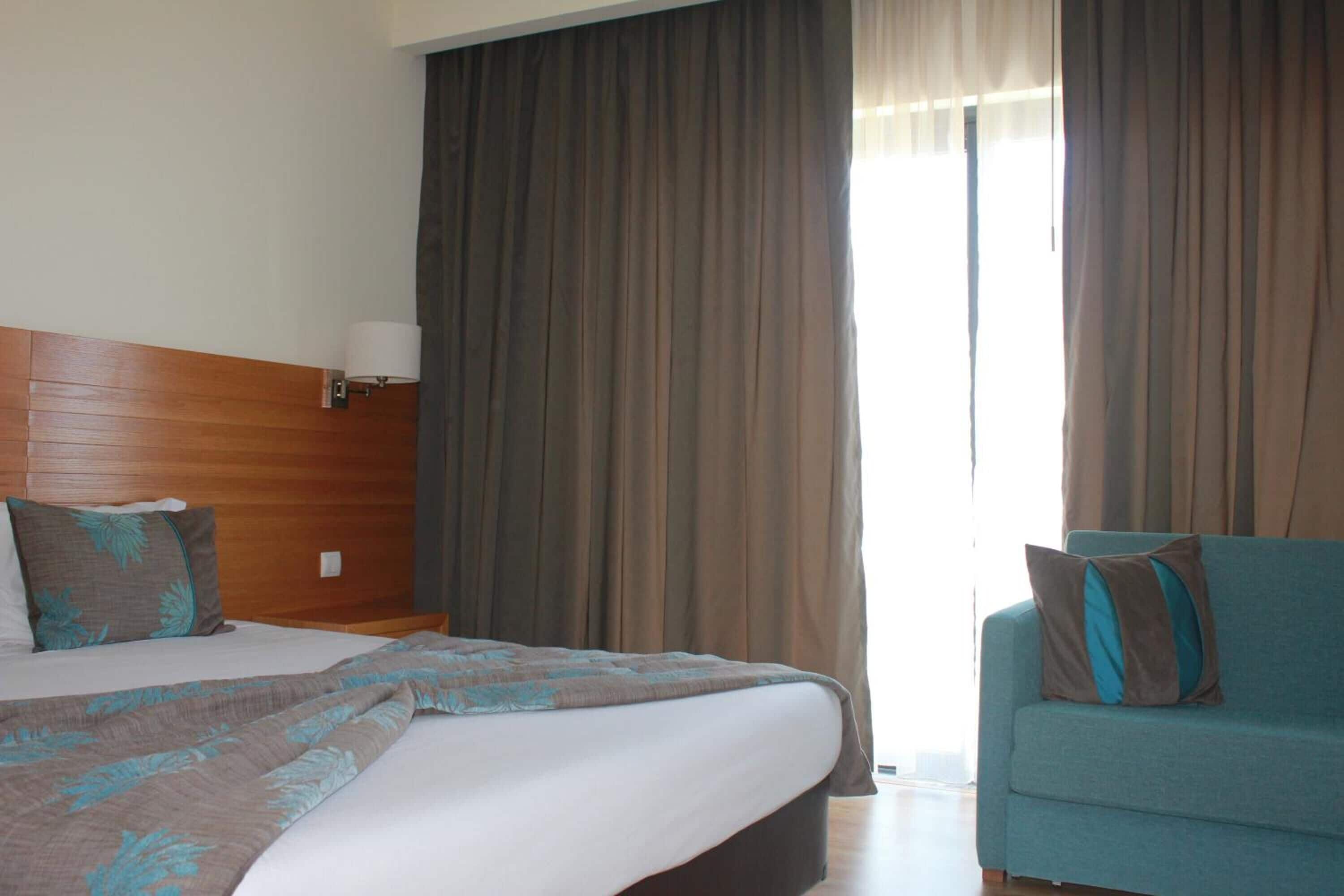 A hotel room with a bed, a sofa, a lamp, and curtains.