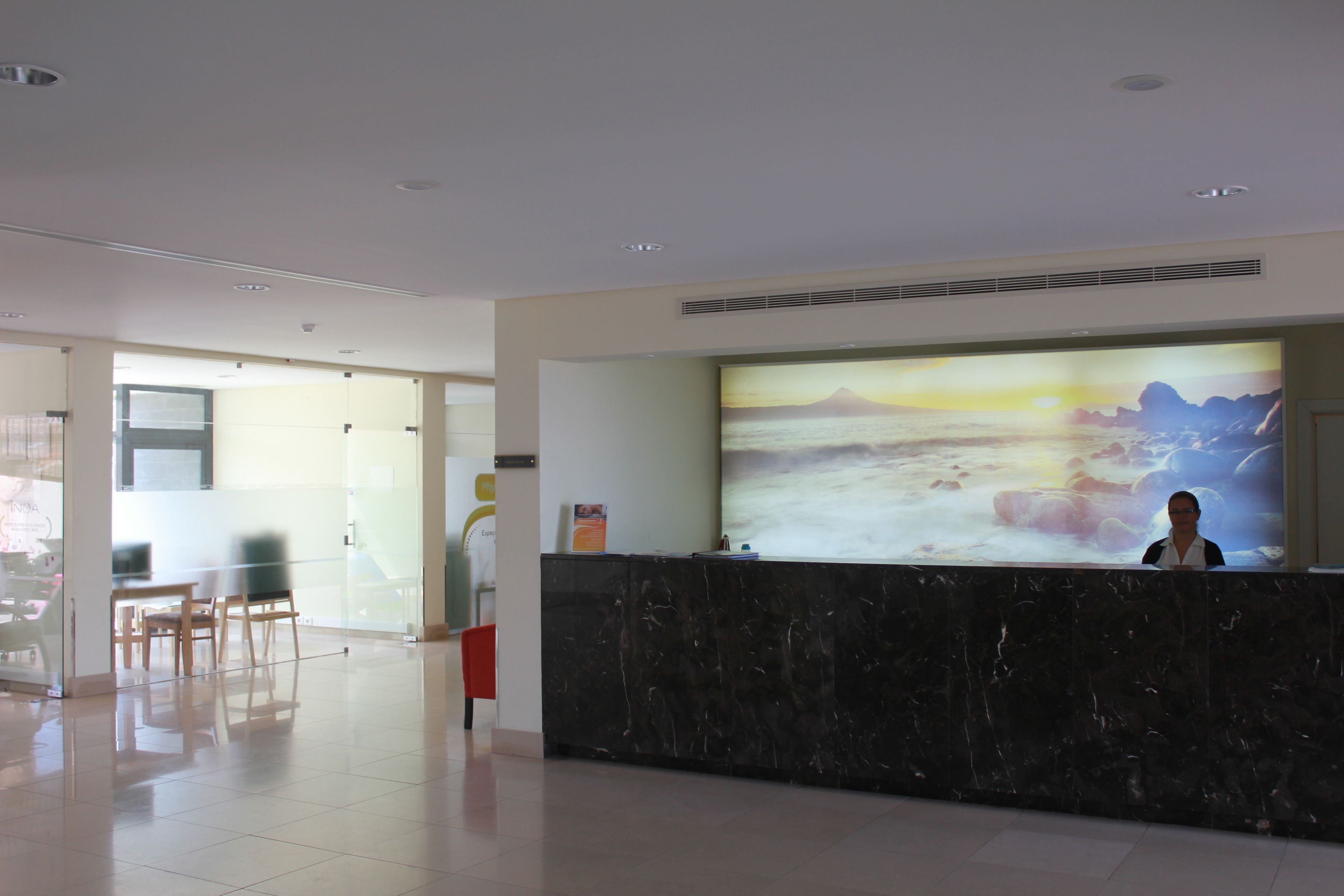 A hotel reception area with a large digital screen displaying a scenic image, a marble reception desk, and a glass partition separating the reception from the adjacent room area.