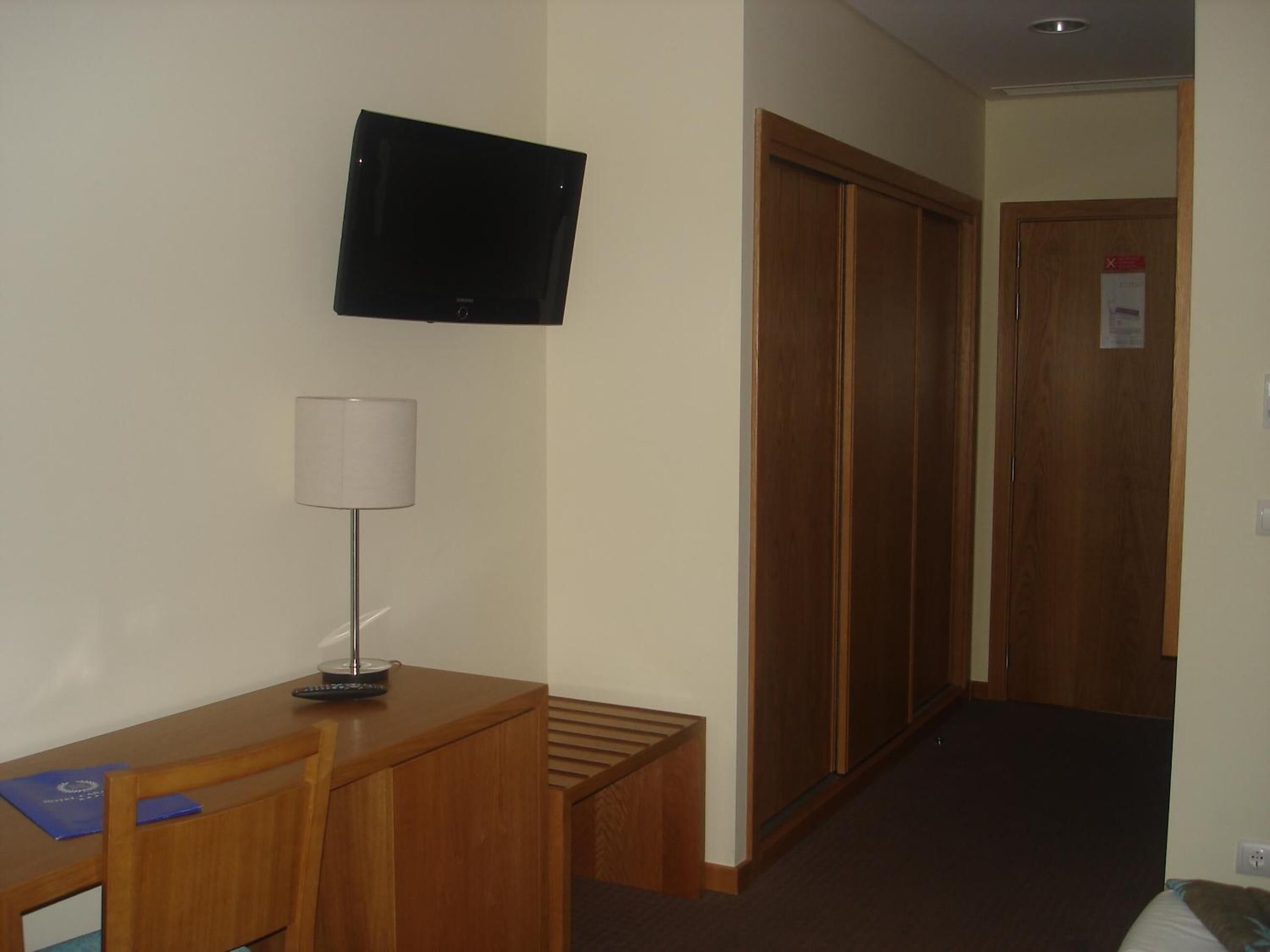 Una camera d'albergo con una scrivania, una sedia, una lampada, una TV e un armadio.