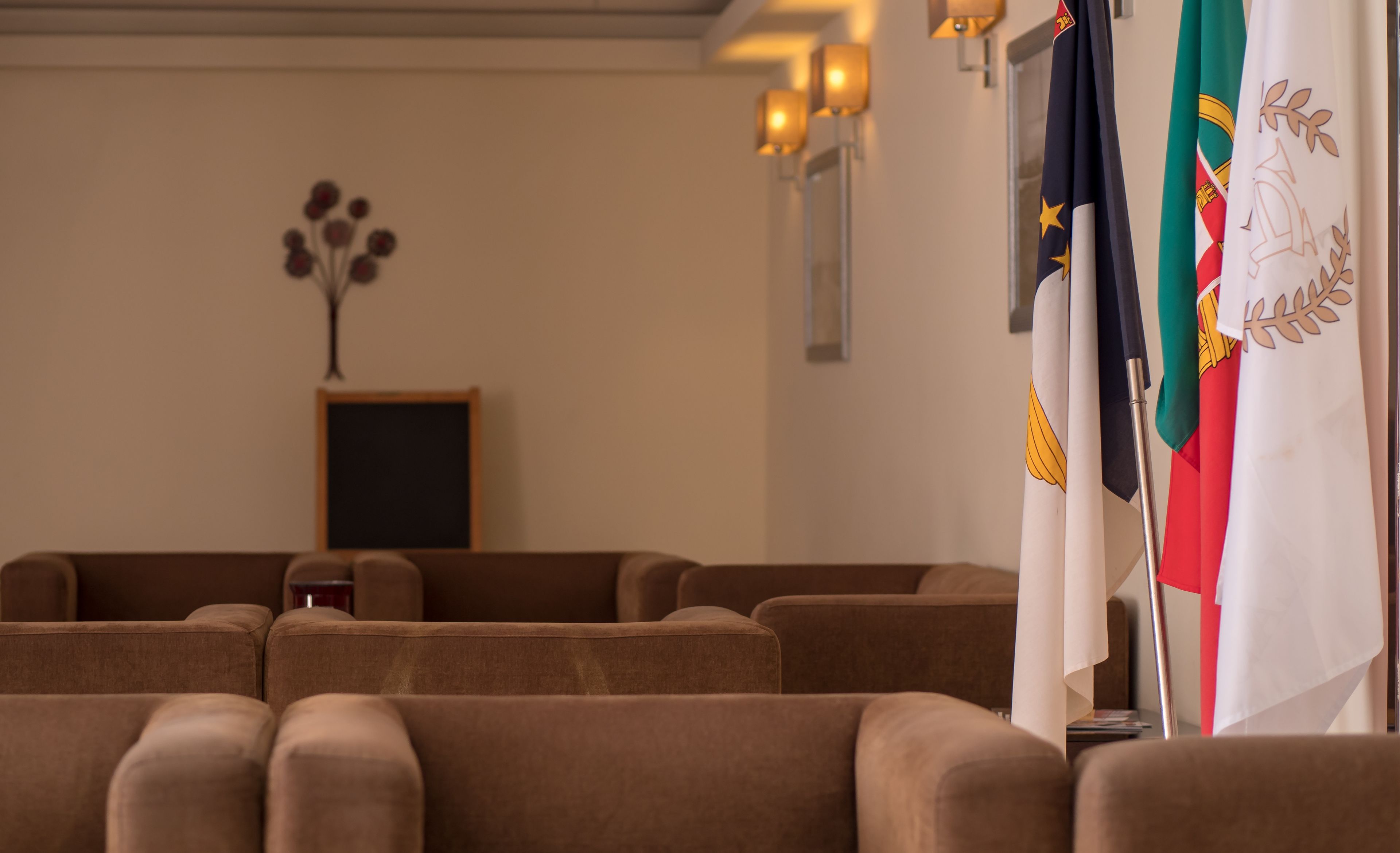 Uma sala de conferências com fileiras de cadeiras marrons, um quadro negro e bandeiras nas paredes.
