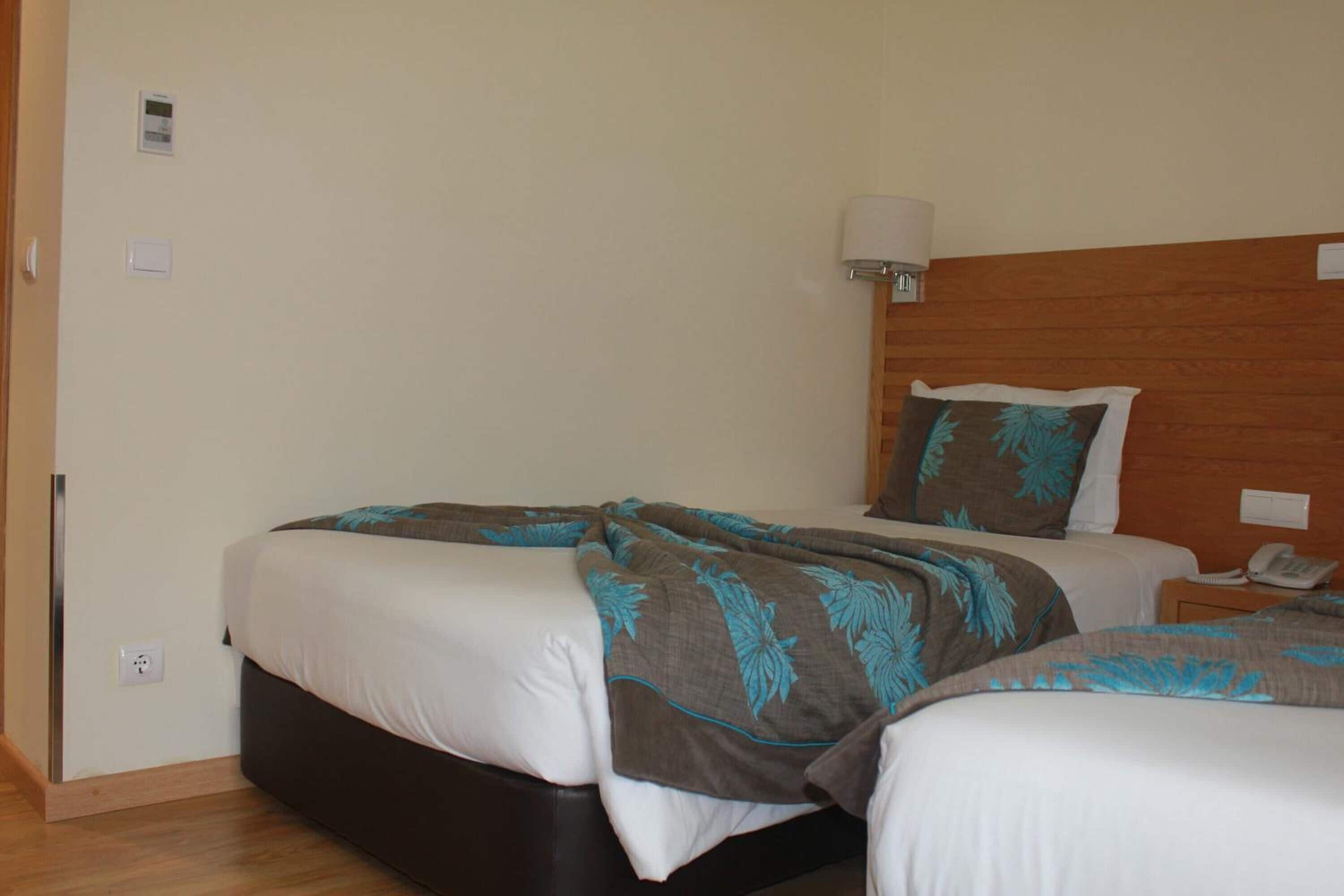 A hotel room with two beds, a wooden headboard, a bedside lamp, and a phone on the nightstand.