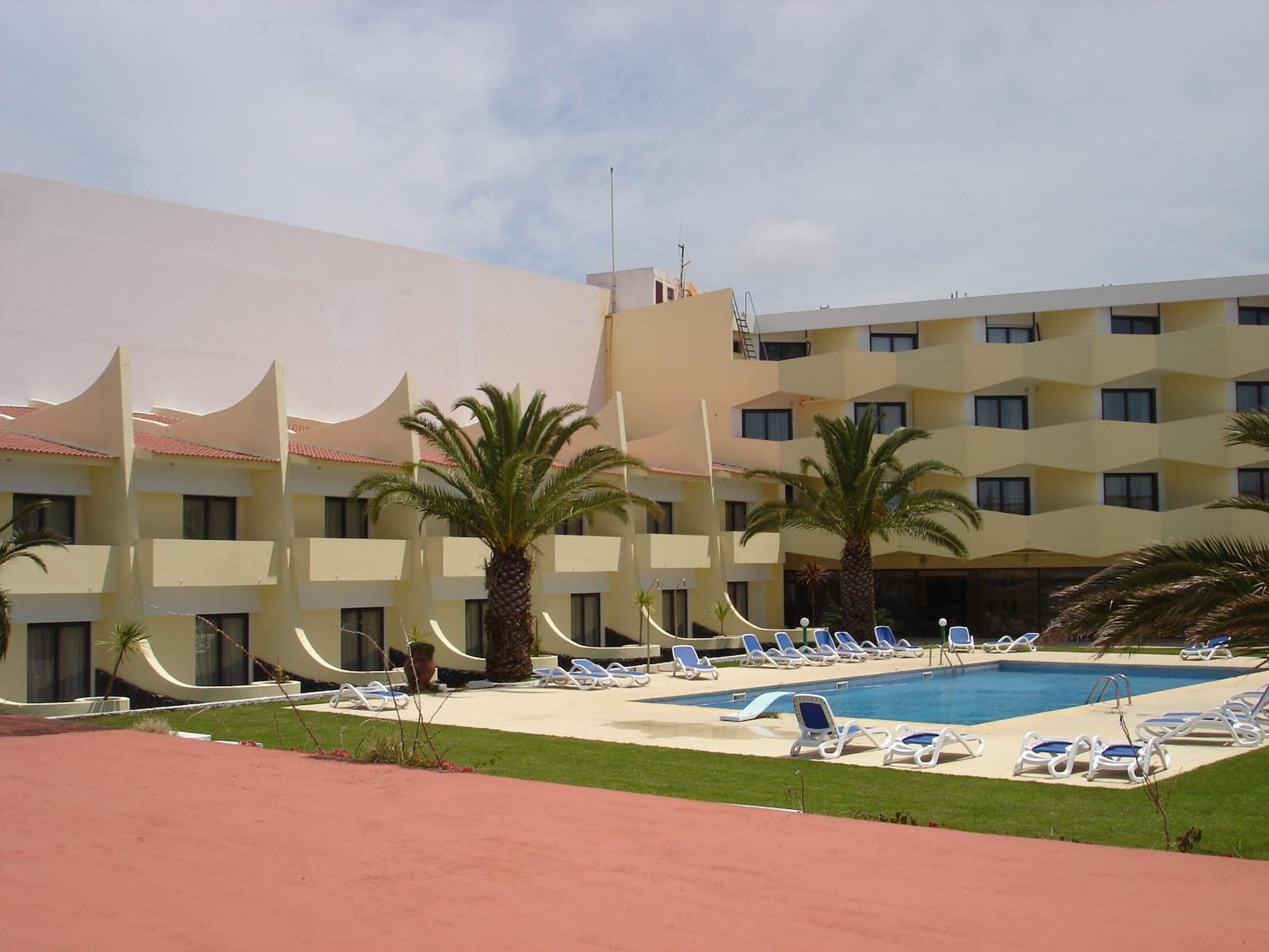 A hotel with a swimming pool, palm trees, and sun loungers.