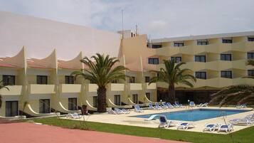 A hotel with a swimming pool, palm trees, and sun loungers.
