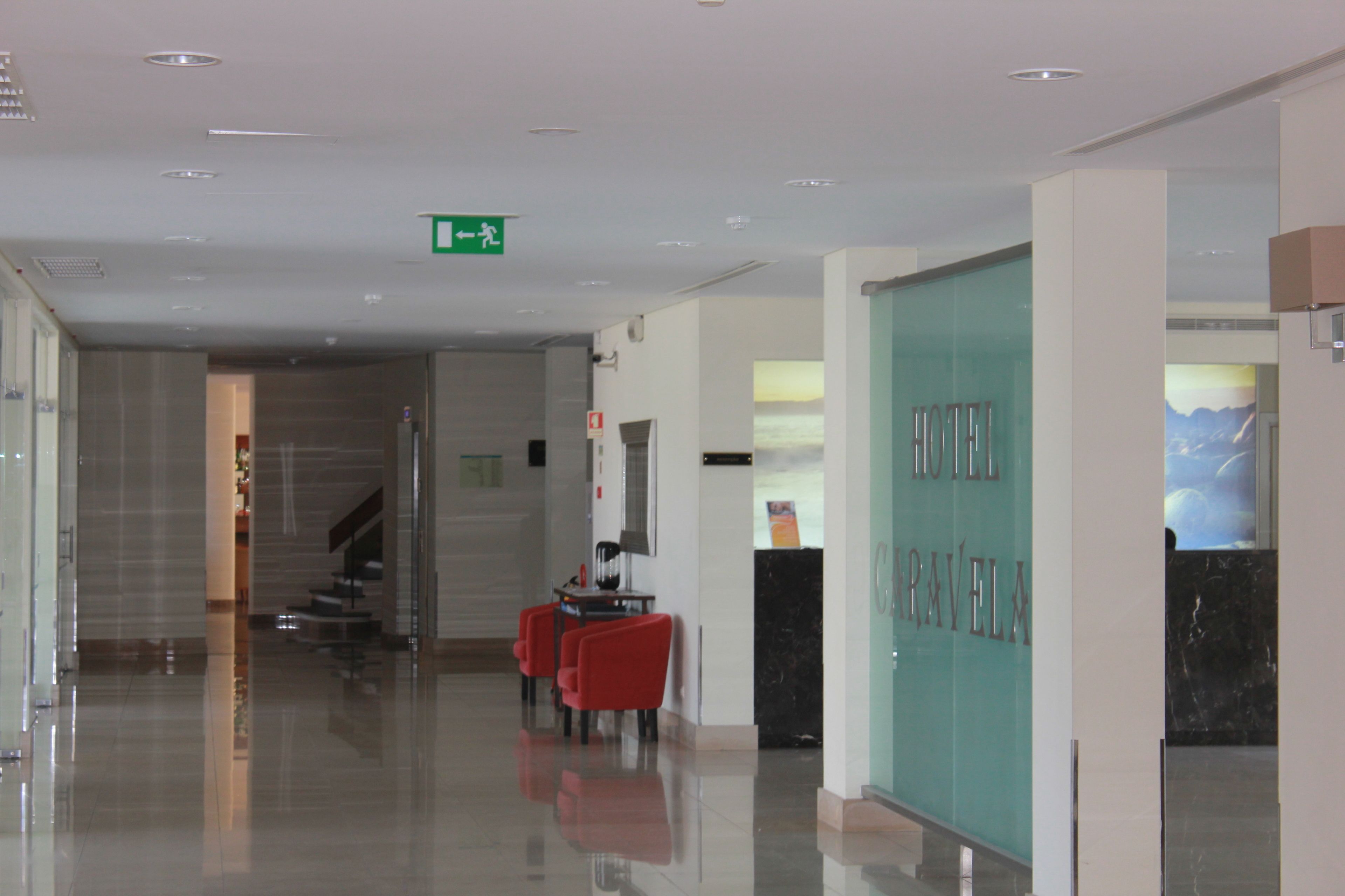 A hotel lobby with a glass wall, a staircase, and red chairs.