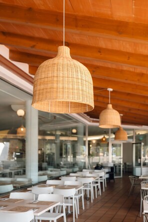 A restaurant interior with multiple tables and hanging wicker pendant lights. - Bluesea Marina Parc (Mercadal)