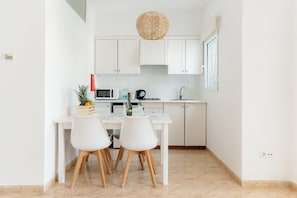 A modern kitchen with white cabinets, a white countertop, and two white chairs with wooden legs. - Bluesea Marina Parc (Mercadal)