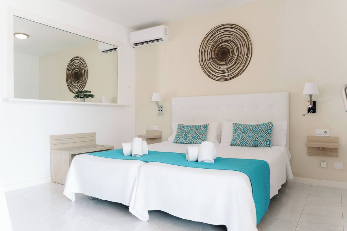 A hotel room with a large bed, a mirror, two wall-mounted lamps, and a wall decoration.