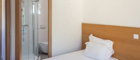 A hotel room with a bed, a wooden headboard, a bedside table, and a glass-enclosed shower area.