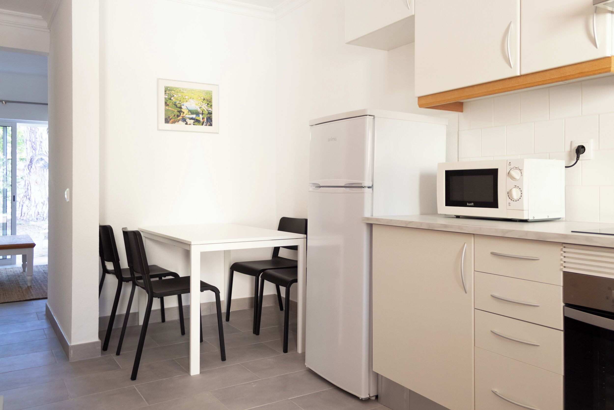 A modern kitchen with white cabinetry, a white refrigerator, a microwave, and a dining area with a white table and black chairs.